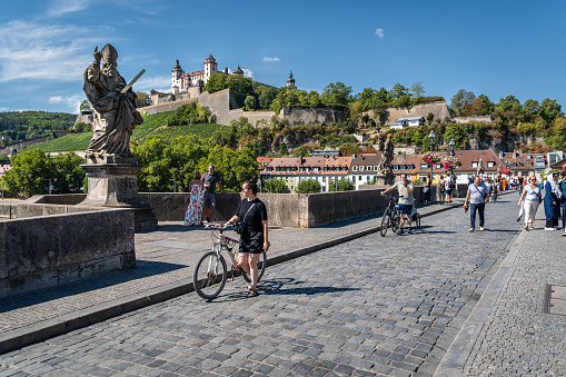 People enjoying a summer day at Wurzburg Old Bridge with Marienberg Fortress in the background. Wurzburg, Bavaria, Germany, Aug. 2022