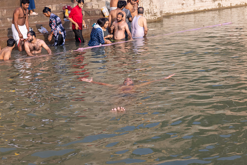 Varanasi, Uttar Pradesh, India - November 2022: Brahmin male swimming in river ganges as hindu ritual during morning.