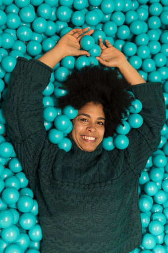 Vertical portrait with top view of a Happy African woman lying on a pool of green plastic balls