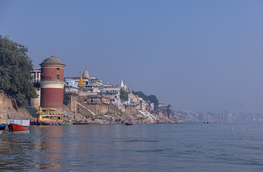 Varanasi, Uttar Pradesh, India - November 2022: Historic Varanasi city with ancient temples and buildings architecture along the ganges river ghat as viewed from a boat during sunrise.