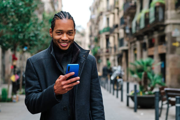 istock Man looking at camera and smiling while holding mobile phone standing on the street. 1482347583
