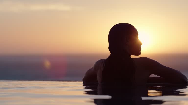 woman relaxing in swimming pool at luxury hotel spa enjoying beautiful golden sunset view of ocean meditarranean travel holiday resort female silhouette 4k