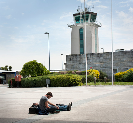 A Coruña, Spain_ May 12, 2012: Control tower of La Coruña airport, two young male passengers resting outside passengers terminal.