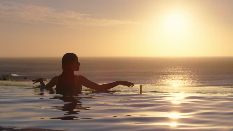 woman relaxing in swimming pool at luxury hotel spa enjoying beautiful sunset view of ocean meditarranean travel holiday resort 4k