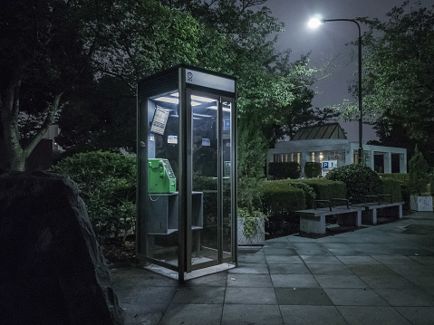 A serene, urban oasis: a glowing, public phone booth illuminates the quiet Aoyama Cemetery in Minato City, Tokyo, beckoning you to escape to its peaceful surroundings