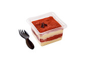 Tiramisu dessert in a plastic box with a fork on a white background