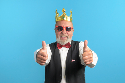 Funny old man in a festive suit on a blue background with a bow tie and a golden crown on his head
