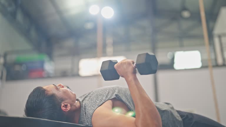 Young sporty woman is having weight training with dumbbells at the gym with assistance of instructor