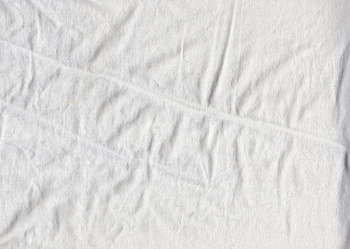 The texture of the cotton fabric of the sheet with slight folds and wrinkles over the entire surface. The folds are arranged in a chaotic order