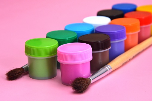 Row of paint pots in a variety of colors, most of which are primary. The pots have seen lots of use, perhaps by a very creative person. Focus on nearest two rows.