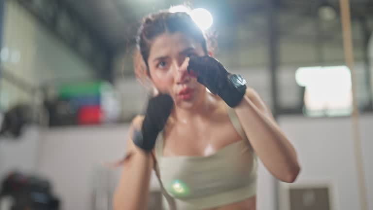 Young Woman With Gloves doing exercise boxing and body bending In A Gym