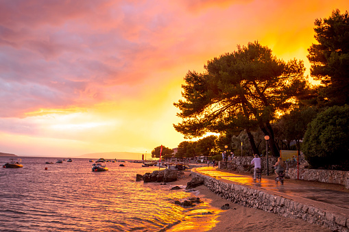 Cres, Croatia - July 7, 2022: People take a bicycle ride along the beach path from the city of Cres before the sunset.