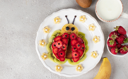 Funny pancakes in the form ladybug with strawberry, banana and kiwi for kids breakfast, Top view