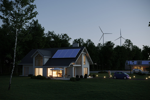 Modern designed energy efficient house with solar panels wind turbines behind it and an electric car in front of the house, representing sustainable lifestyle, evening scene. Charging station and concept cars are not based on any real ones. (3d render)