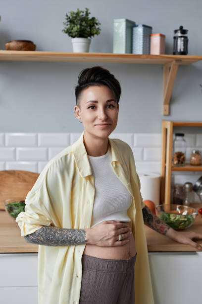 istock Tattooed pregnant woman looking at camera standing in kitchen 1482392230