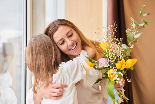 mother and daughter hugging with flowers - family, child, holiday and party concept