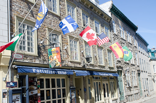 Line-up of local and international flags above Portofino restaurant entrance during springtime day in Quebec city