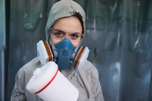 portrait of pest control worker standing in respirator and holding sprayer in kitchen