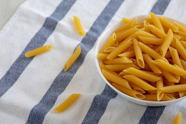 Homemade Raw Dry Penne Pasta in a White Bowl, side view. Copy space.