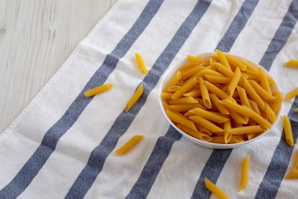 Homemade Raw Dry Penne Pasta in a White Bowl, low angle view. Space for text.