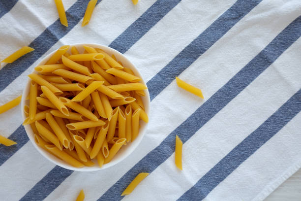 Homemade Raw Dry Penne Pasta in a White Bowl, top view. Flat lay, overhead, from above. Space for text.