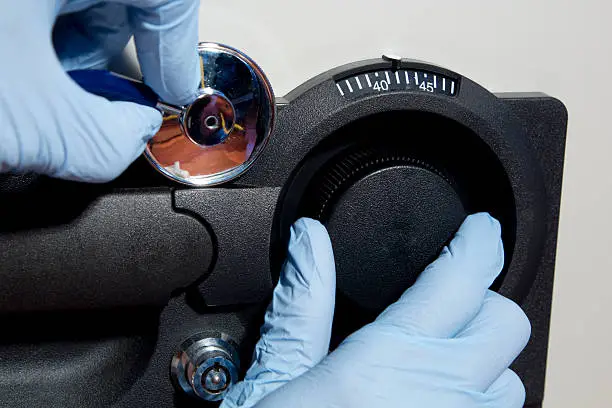 Horizontal image of a safe being cracked by a theif wearing gloves using a stethoscope.