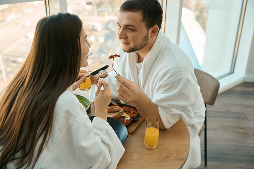Spouses in love chat nicely over breakfast in a cozy atmosphere, guys in soft bathrobes