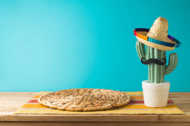 istock Empty wooden table with wicker place mat  and cactus decoration over blue wall  background. Mexican party mock up for design and product display 1482411965