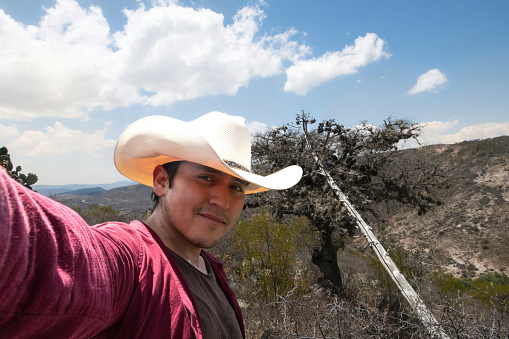 A man in a cowboy hat takes a selfie in front of a mountain.