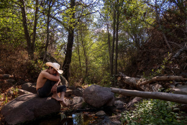 istock Man sits on a rock in a forest, wearing a cowboy hat. 1482429469