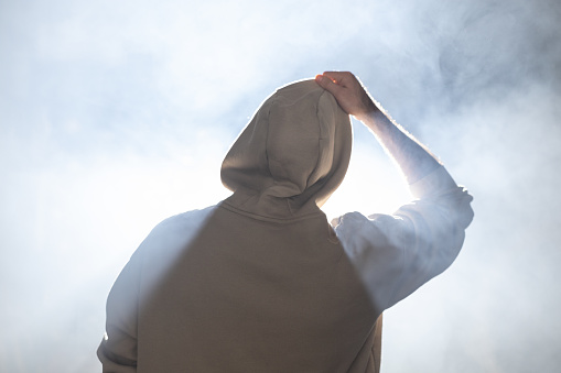 Unrecognizable modern man in hooded shirt standing in smoke.