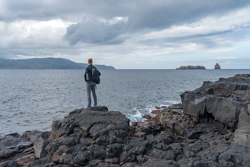 One tourists on black volcanic lava field by the sea, island Pico, Azores