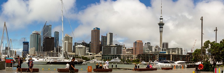 Auckland, New Zealand - January 28, 2023 :  Panorama of tourists along waterfront with skyline of Auckland, New Zealand against cloudy blue skies with copy space.
