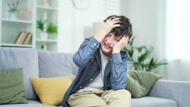 Teen child with tension, boy suffering from headache sitting on couch at home