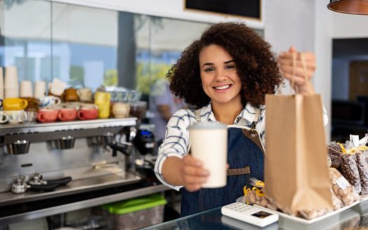 Happy Latin American waitress selling Take Out Food at a coffee shop and looking at the camera smiling