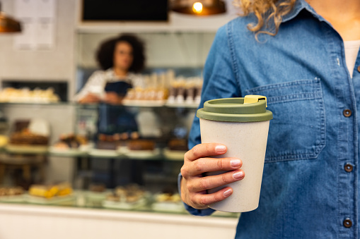 Close-up on a customer buying a cup of coffee to go and holding a reusable cup while leaving the shop
