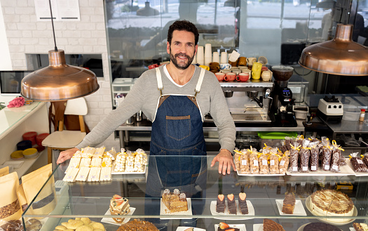 Happy business owner smiling behind the counter at a coffee shop and looking at the camera - food service occupation concepts