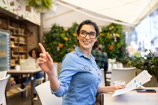 Latin American woman calling a waitress at a coffee shop - lifestyle concepts