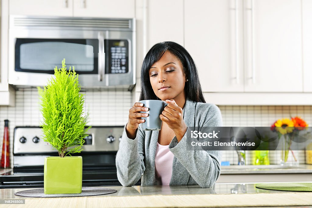 Woman in kitchen with coffee cup Thoughtful black woman holding coffee mug in modern kitchen interior Adult Stock Photo