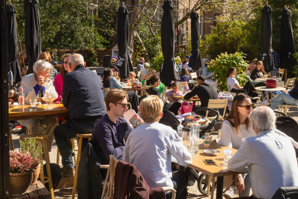 People enjoy the spring sun on the terrace of the restaurant Vondeltuin in the Vondelpark in Amsterdam. Amsterdam, The Netherlands, March 27, 2022; People enjoy the spring sun on the terrace of the restaurant Vondeltuin in the Vondelpark in Amsterdam. busy restaurant tables stock pictures, royalty-free photos & images