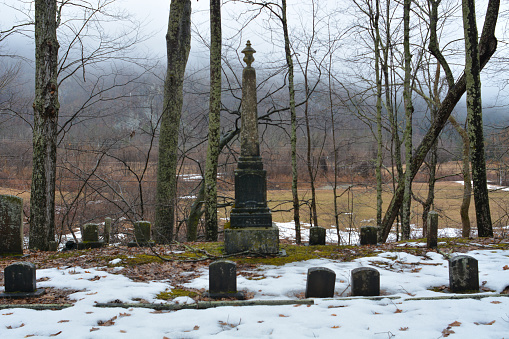 A tall obelisk monument stands amongst a collection of small headstones on winter day in New England.
