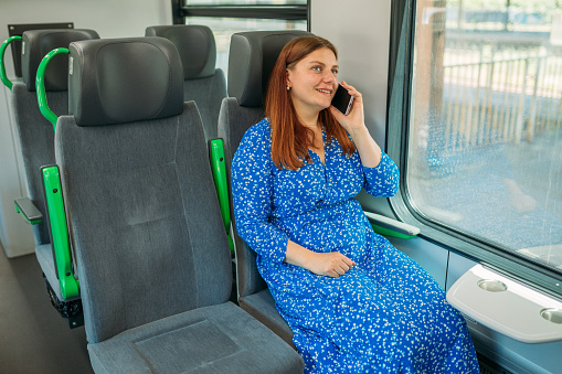 Happy Redhead woman talking on the mobile phone and sitting in the modern train, Railroad transport concept