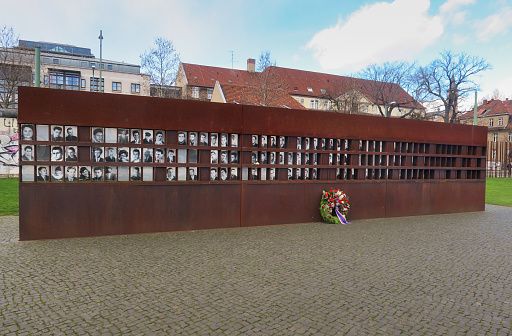 wreath of flowers in front of the memorial to people who were killed trying to escape East Germany at the Berlin Wall, with their photographs inset into the monument.