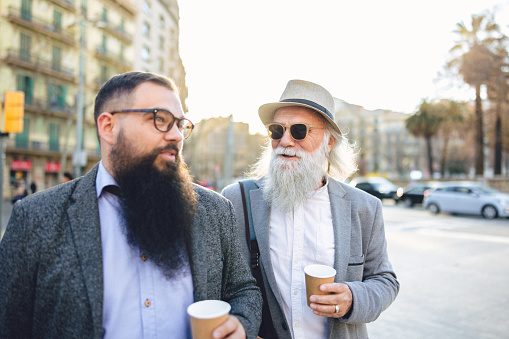 Two bearded business casual men in the street of Barcelona, next to the Tetuan square.