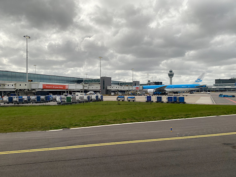 A view from a passenger window of a landed commercial flight taxiing around the airport of Schiphol in Amsterdam, the Netherlands. Architecture of the airport terminal buildings can be seen along with parked commercial flights at boarding gates