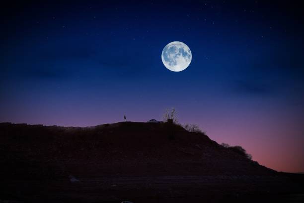 istock A moon is seen above a hill, man watching the sky alone on the hill. 1482484633