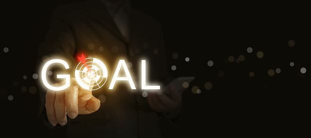 Hit Your Targets with Precision: Unleash Your Business Potential with the Power of Goal Setting. A Businessman's Hand Points to the Glowing Word 'GOAL', with the Letter 'O' as a Dart Target Board.