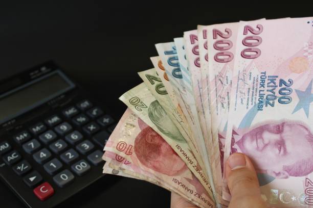 A person holds a stack of turkish banknotes in front of a calculator.