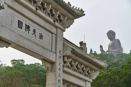 A stone archway in Ngong Ping Village. In the background the Tian Tan Buddha Statue. Lantau Island. Hong Kong.