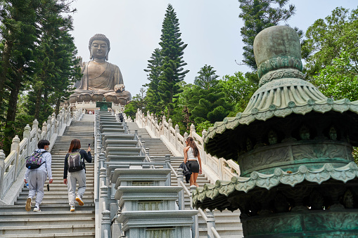 Ngong Ping, Hong Kong - April 15, 2023: tourists climbing the stairs that bring to Tian Tan Buddha monument, a large bronze statue of Buddha Shakyamuni, located on top of Ngong Ping on Lantau Island. Hong Kong.
